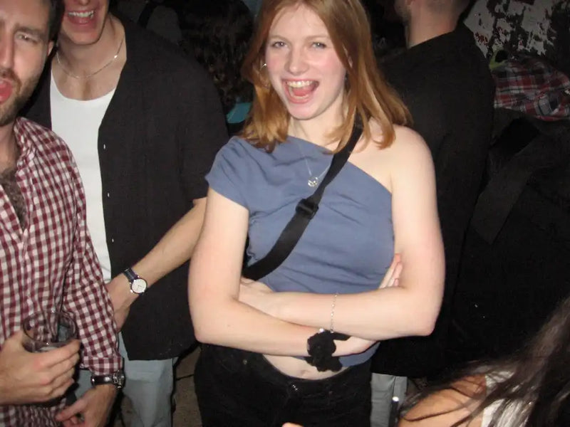 Woman in a blue top and black pants standing among people at a swim club dance event