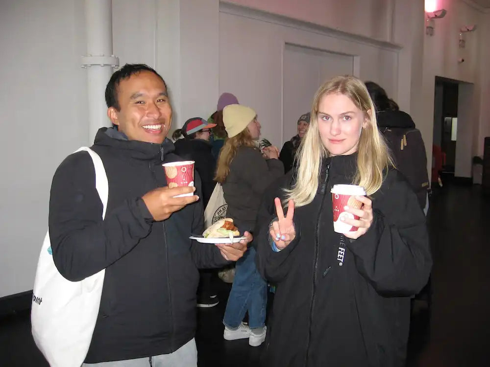Two swimmers holding coffee cups and a plate with food in an indoor setting socialising after swim club in London