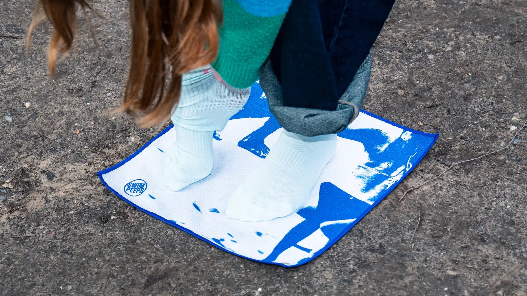 A person changes their socks on the Swim Peeps Dry Step Swim Changing Mat