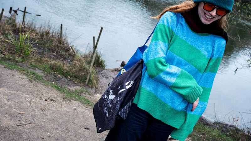Young urban swimmer standing near a swimming pond in London with a Swim Peeps Dry Step Swim Changing Mat hanging from their tote bag