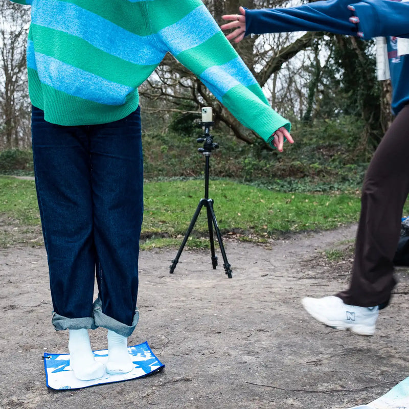 Two people outdoors, one stepping onto a Swim Peeps Dry Step Swim Changing Mat